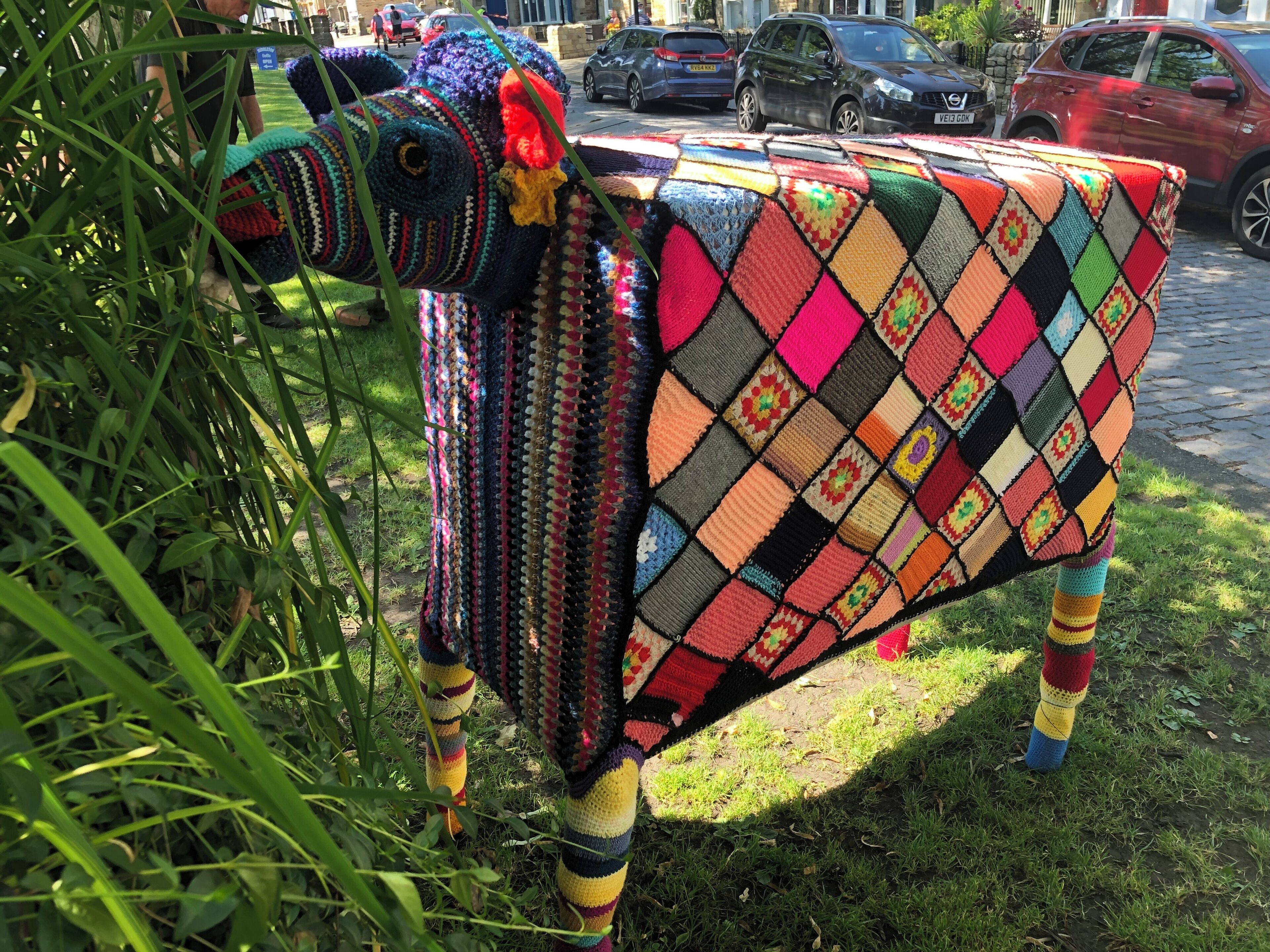 Una scultura di un animale colorato, realizzata all'uncinetto, con un motivo a scacchi sul dorso, posizionata sull'erba.