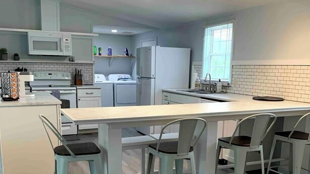 Une cuisine moderne dotée d’un îlot central, de meubles blancs et d’un coin repas avec quatre chaises.