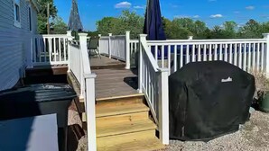 Une terrasse en bois avec une balustrade blanche, un barbecue abrité et une statue.