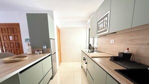 A modern kitchen with green cabinets, a wooden countertop, and a microwave above the sink. - La Esterlicia (Los Abrigos)