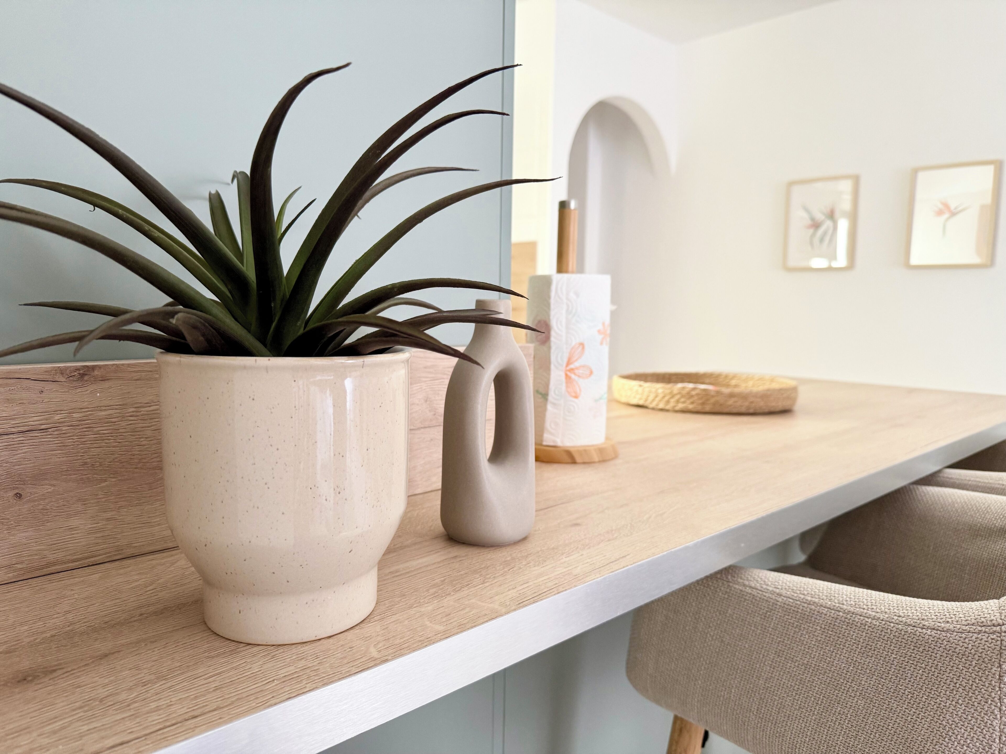 Una repisa de madera con una planta en maceta, una taza de cerámica y un rollo de papel higiénico.