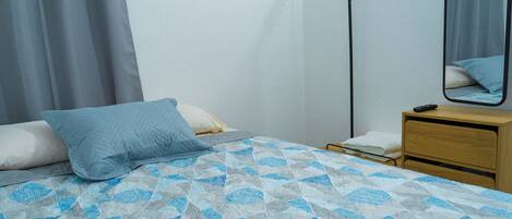 A neatly made bed with a patterned bedspread, a bedside table with a lamp, and a mirror on the wall.