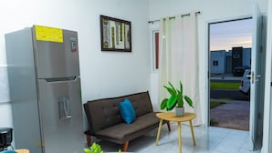 A compact living space with a refrigerator, sofa, small table, and potted plant. - Casa Oriente (San Miguel)