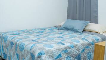 Una cama individual con una colcha estampada, cabecera gris y cortina gris.