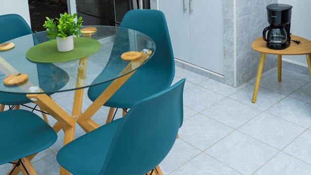 A modern kitchen with a dining area, featuring a glass table, teal chairs, and a small coffee table. - Casa Oriente (San Miguel)