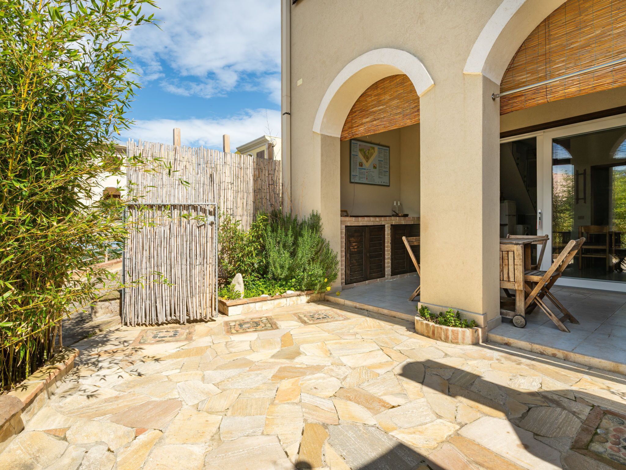 A stone-paved patio with a wooden fence, a wooden table and chairs, and a covered outdoor area with a view of the surrounding landscape.