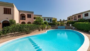 En swimmingpool med kristallklart blått vatten, omgiven av byggnader med balkonger och välvda fönster.