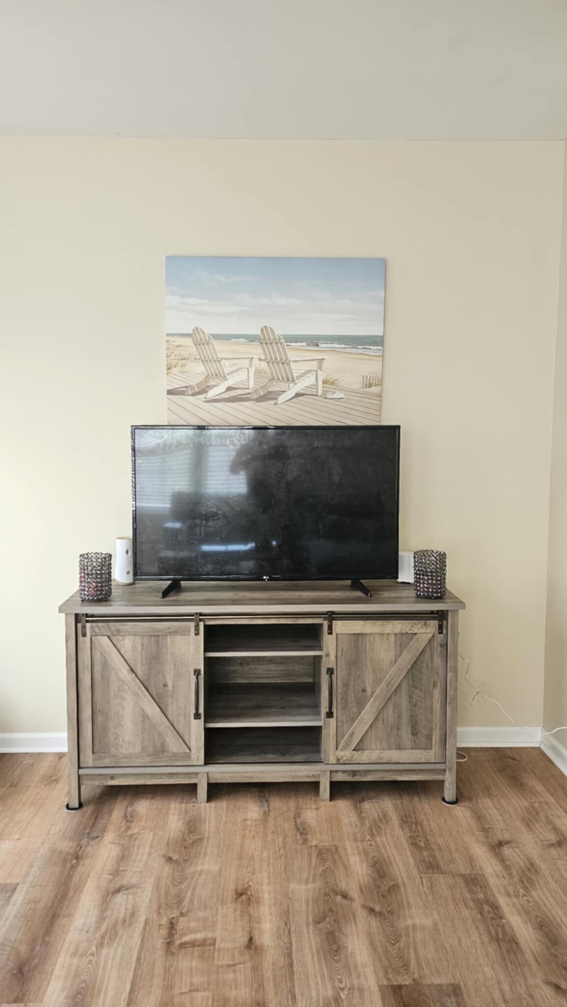 Et fladskærms-tv på et træskab med to sengeborde, et maleri af et strandmotiv over, og en trægulv.