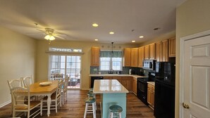 A kitchen with wooden cabinets, a black refrigerator, a microwave, and a dining area with a wooden table and white chairs. - 4bedroom Beach Retreat in charming Long Neck with Rooftop View and lounging deck (Long Neck)