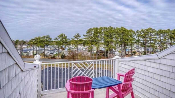 A balcony with a view of a residential area, featuring a table and two chairs. - 4bedroom Beach Retreat in charming Long Neck with Rooftop View and lounging deck (Long Neck)