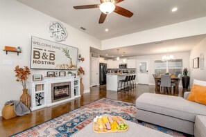 A spacious living room with a fireplace, a dining area, and a kitchen in the background.