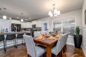 A modern kitchen with white cabinets, a wooden dining table set for four, and a large potted plant.