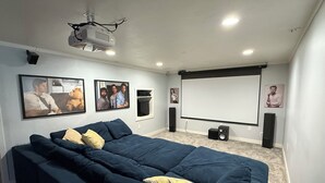 A home theater room with a large screen, ceiling-mounted projector, and a dark blue sofa. - Fun, Cosy, Theater Basement! (Lehi)