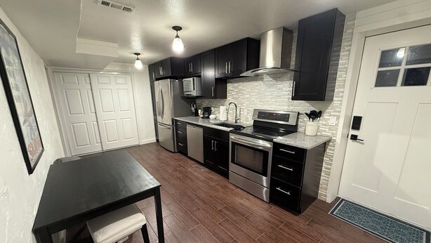 A modern kitchen with stainless steel appliances, dark cabinetry, and a tiled backsplash. - Fun, Cosy, Theater Basement! (Lehi)