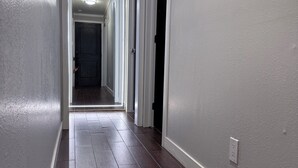 A hallway with dark wooden flooring, white walls, and a ceiling light. - Fun, Cosy, Theater Basement! (Lehi)