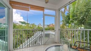 A balcony with a glass table, a chair, and a view of a residential area with houses and a bridge.