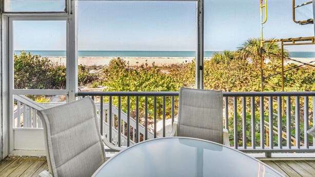 A balcony with a glass door leading to a beach view.
