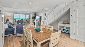 A spacious living area with a wooden dining table, comfortable seating, and a view of the ocean.