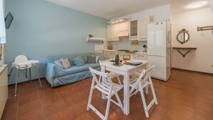 Ett kompakt bostadsutrymme med ett litet kök, en matplats med bord och stolar, en soffa och en liten vit stol.