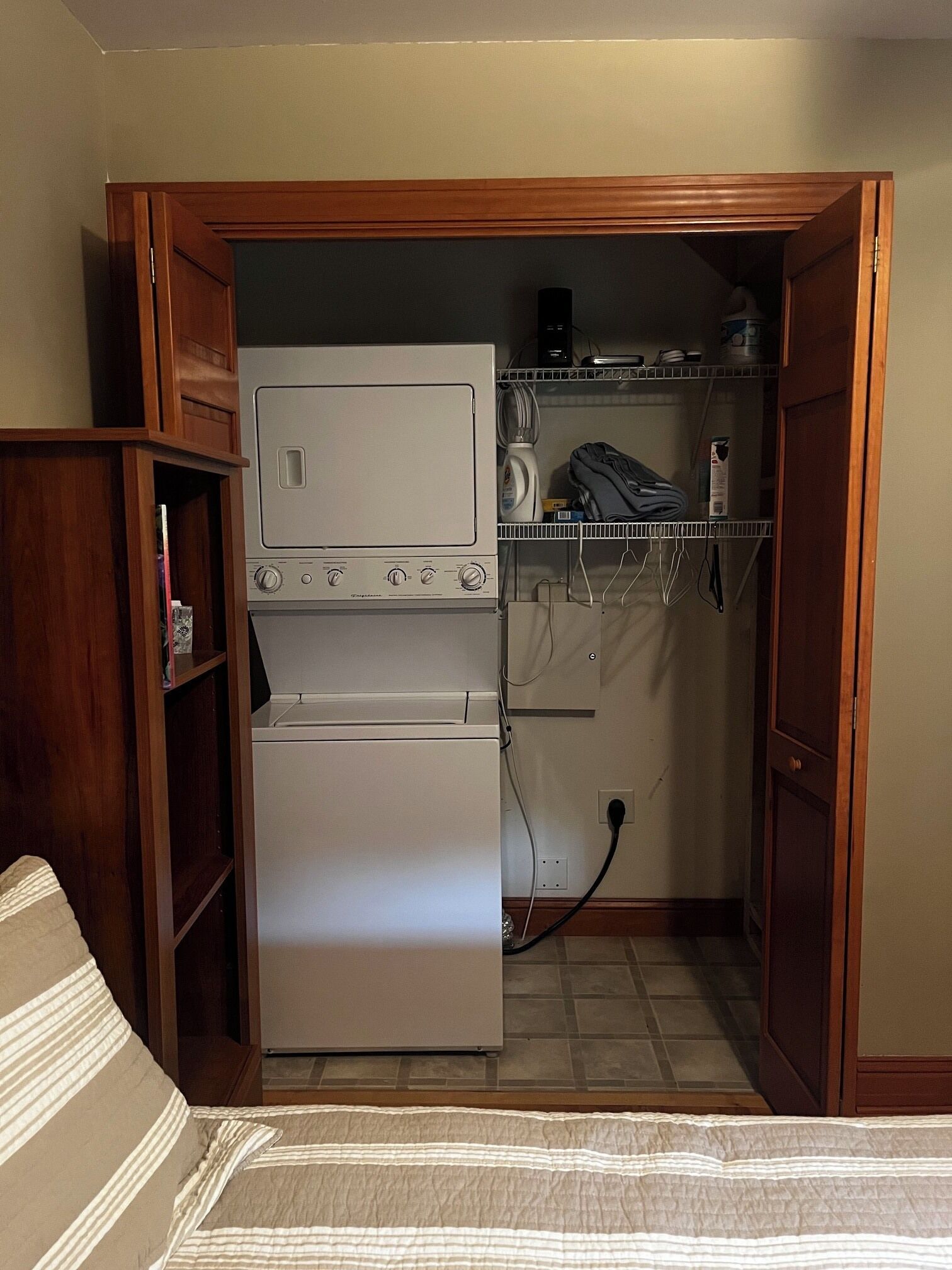 A compact laundry room with a washer and dryer, wooden shelving, and a small cabinet.