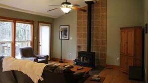 Una sala de estar con chimenea, ventilador de techo y un amplio ventanal.