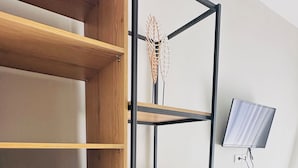 A compact room with a built-in wardrobe, a small refrigerator, a desk with a chair, and a television mounted on the wall. - Luizas Apartments  (Sarandë)
