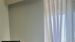 A room with a bed, a standing mirror, a wall with a framed artwork, and sheer curtains. - Luizas Apartments  (Sarandë)