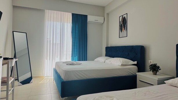 A hotel room with two beds, a desk, a chair, a mirror, and an air conditioning unit. - Luizas Apartments  (Sarandë)