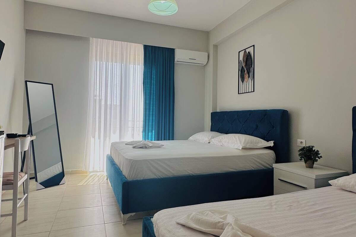 Habitación de hotel con dos camas, un escritorio, una silla, un espejo y un equipo de aire acondicionado.