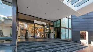 A modern hotel entrance with a glass facade, a sign reading "The Seibel Auckland," and a staircase leading to the lobby.