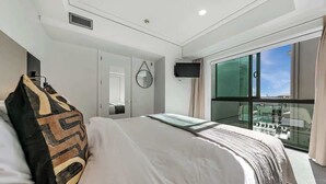 Een moderne hotelkamer met een groot bed, een aan de muur bevestigde televisie en een balkon met uitzicht op de stad.