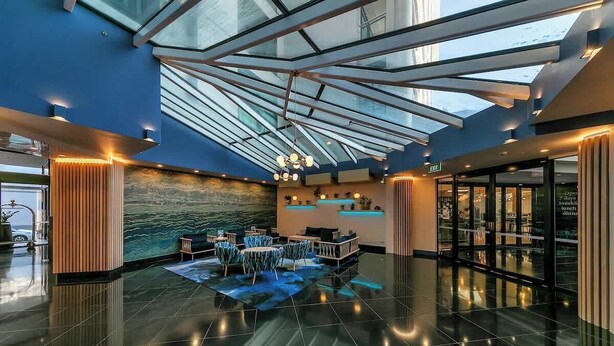 Een moderne lobby met een glazen dak, een receptiebalie, een zithoek en uitzicht op buiten.