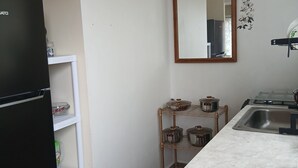 Eine Küche mit einem schwarzen Kühlschrank, einem Spülbecken, einem Spiegel und einem Regal mit Kochtöpfen.