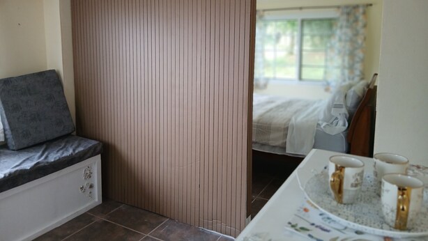 Ein Zimmer mit einem Bett, einem Nachttisch mit Tablett und Tassen, einer Bank mit Kissen und einem Holztrenner.