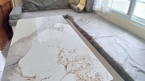 Ein Zimmer mit einem großen Marmortisch, einer eingelassenen Bank mit Kissen und einem Fenster mit durchsichtigen Vorhängen.
