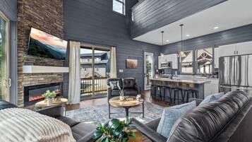 A modern living room with a fireplace, a dining area, and a kitchen with a bar.