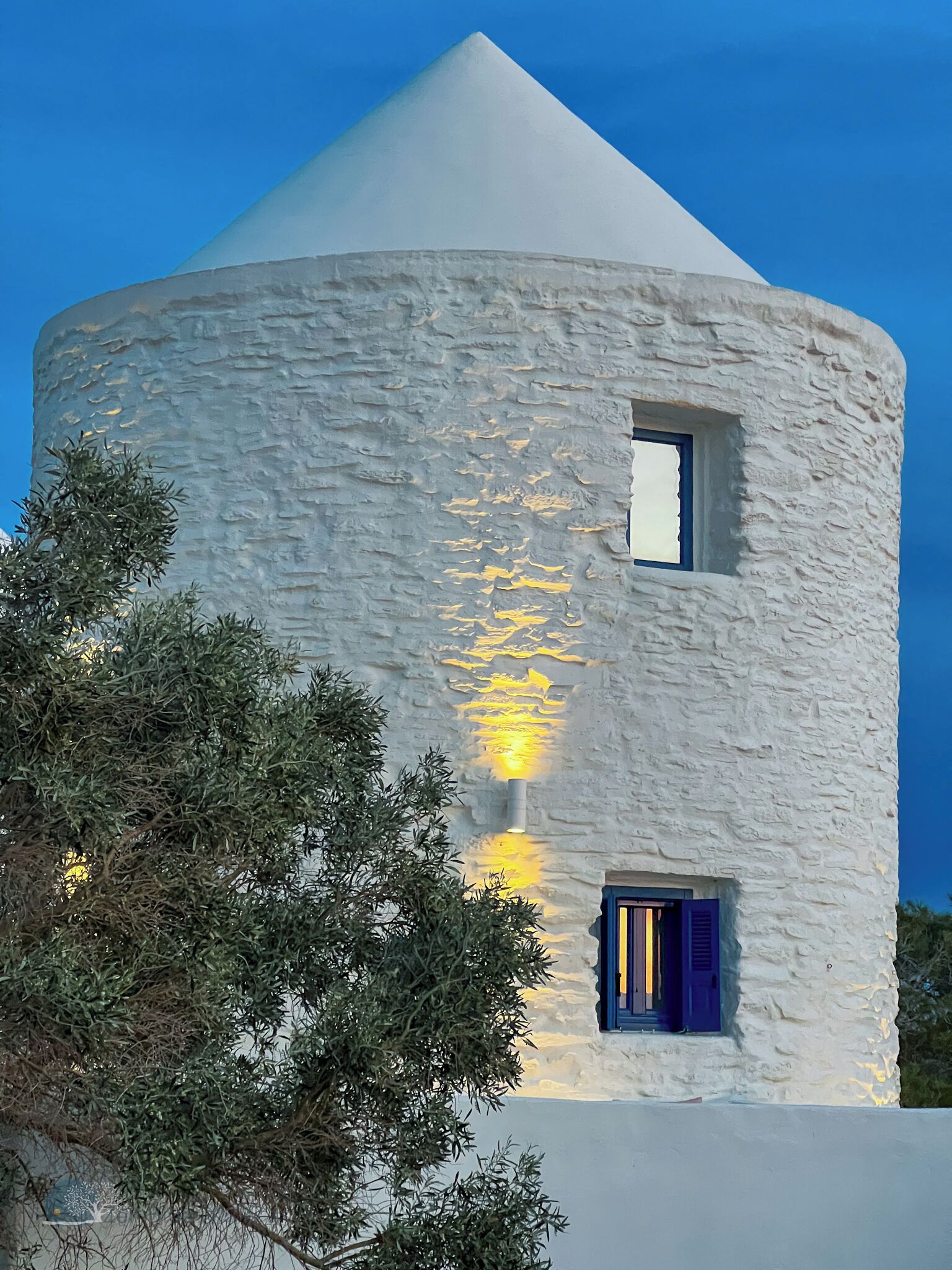 Un edificio blanco con techo cónico y una ventana pequeña con persianas azules.