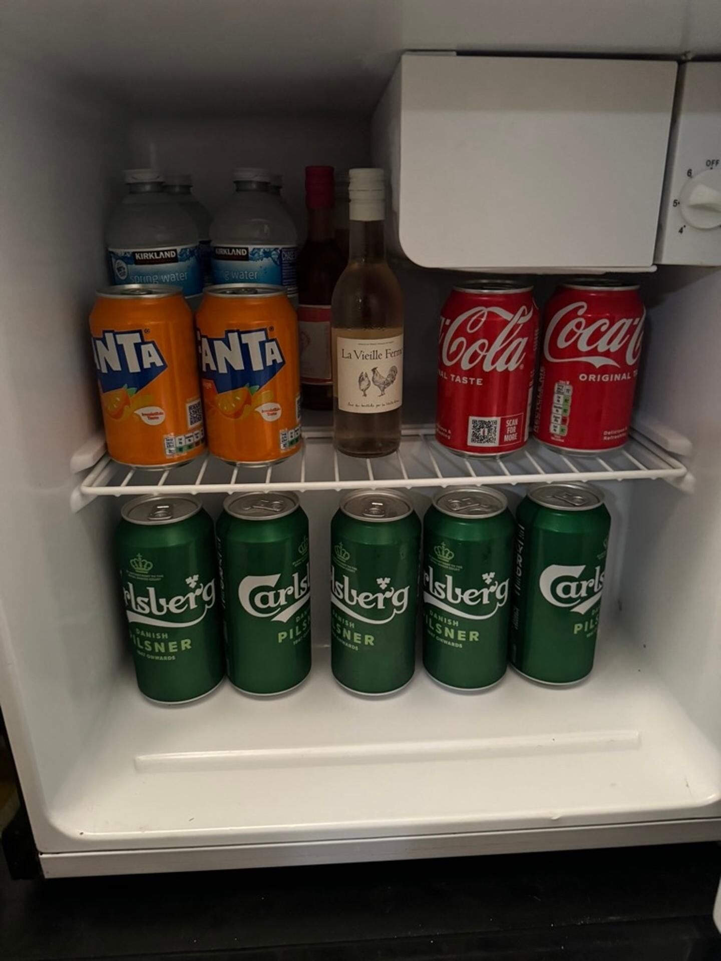 A refrigerator containing various beverages including two cans of Fanta, two cans of Coca-Cola, a bottle of La Vieille Fermi wine, and six cans of Carlsberg beer.