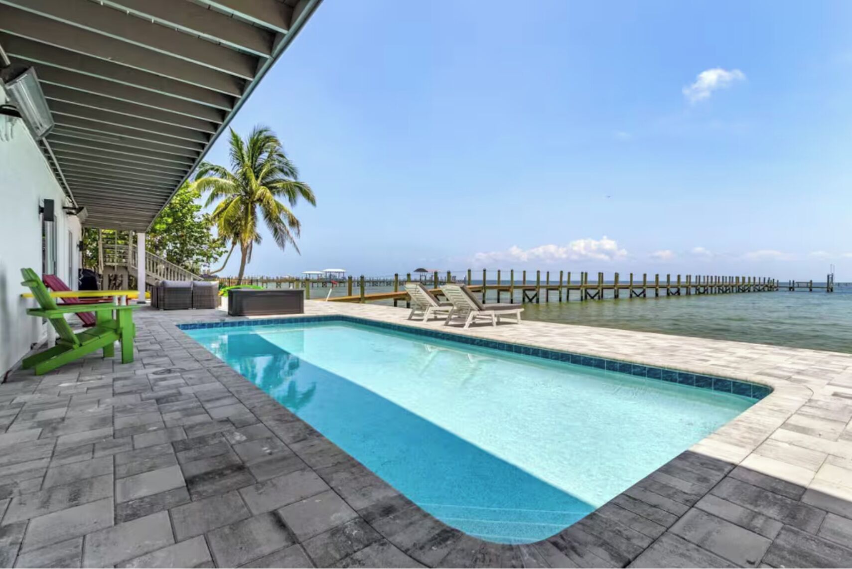A swimming pool with lounge chairs, a covered area, and a view of the ocean and pier.