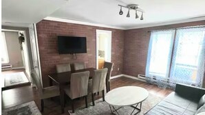 Una sala de estar con pared de ladrillo, un televisor de pantalla plana montado sobre una mesa de comedor, un sofá y una alfombra estampada.