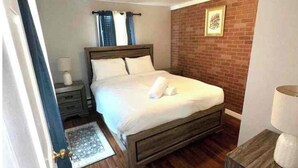 Un dormitorio con una cama de madera, una mesita de noche, una lámpara y una pared decorativa de ladrillo.