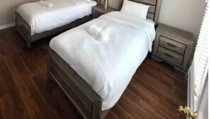 Habitación de hotel con dos camas individuales, cabeceros de madera, mesitas de noche con lámparas y una puerta blanca.