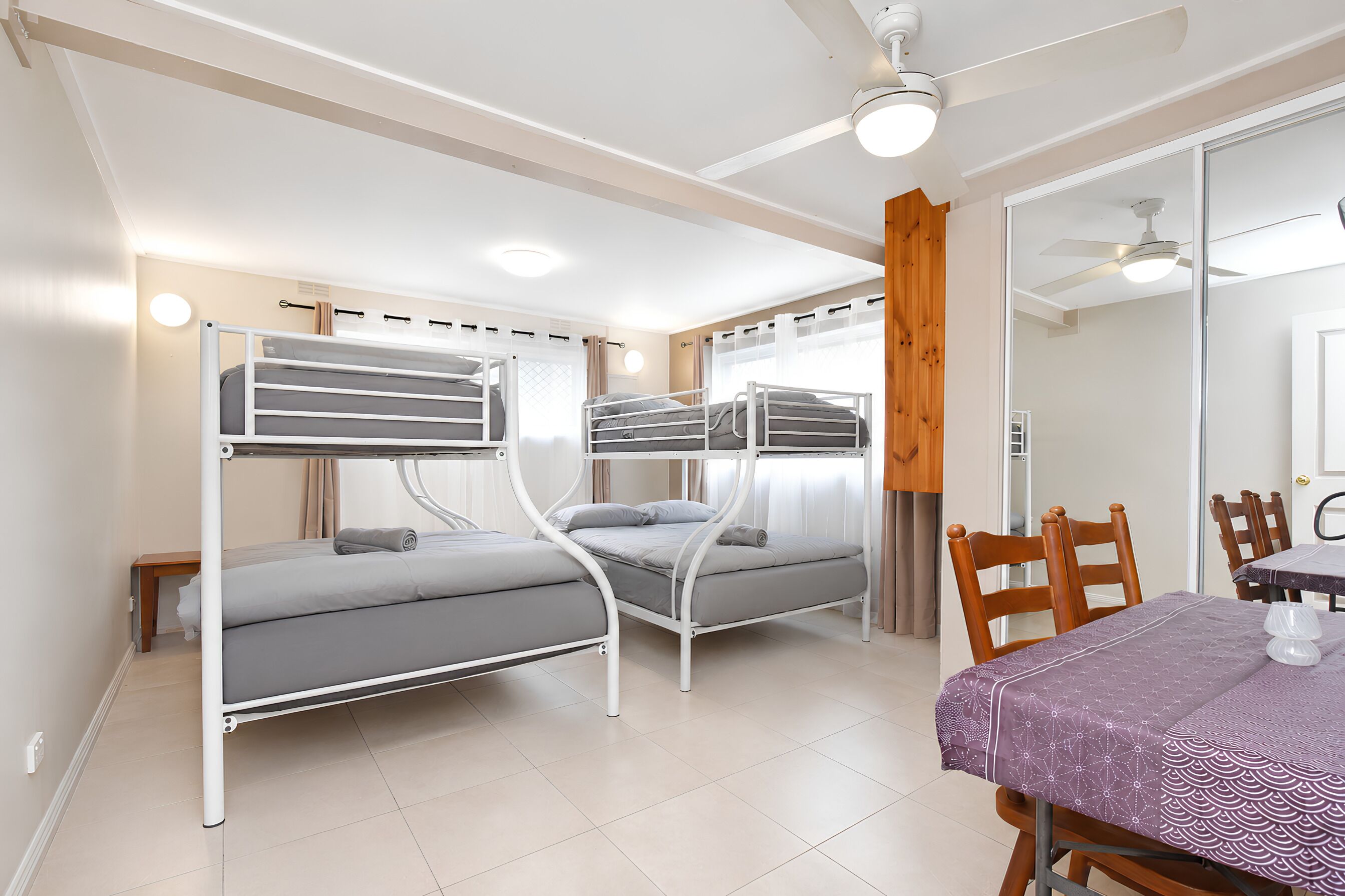 A room with bunk beds, a dining table with chairs, and a ceiling fan.