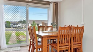 Comedor con mesa y sillas de madera, una planta en maceta y vista al exterior por una puerta de cristal.