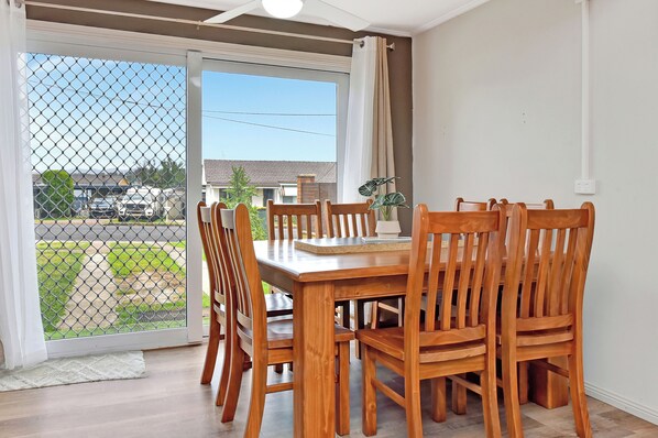 A dining area with a wooden table and chairs, a potted plant, and a view through a glass door to the outside. - Coal d' Vine Chillout - Cessnock NSW (Cessnock)