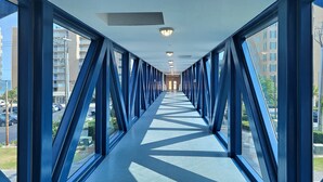 A corridor with a geometric patterned floor, large windows on both sides, and a ceiling with recessed lighting.