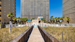 A wooden boardwalk leading to a hotel with a large building in the background.