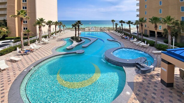 A resort pool with multiple sections, palm trees, and a view of the beach.