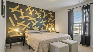 Une chambre à coucher avec un grand lit, des tables de chevet, une commode, une fenêtre avec des rideaux et un mur orné de motifs abstraits.