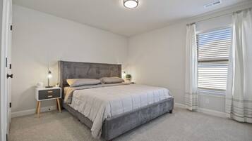 Une chambre à coucher avec un lit, des tables de chevet, une commode, une lampe et une fenêtre avec des rideaux.